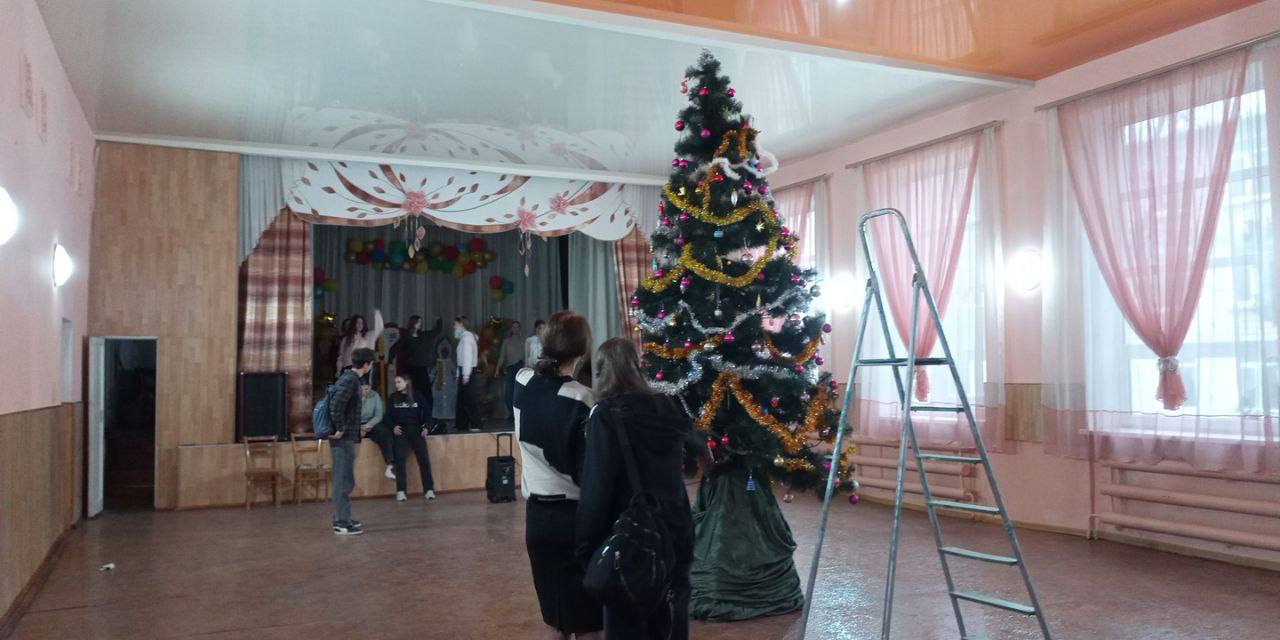 В актовом зале 13-й школы ученики 11 класса нарядили новогоднюю ёлку — главное украшение предстоящих утренников и дискотек
